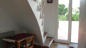 Ein Zimmer mit Holztisch, einem gemusterten Teppich, einer Treppe und einer Tür, die nach draußen führt.