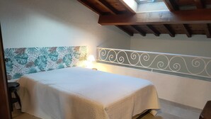 Ein Schlafzimmer mit einem Bett, einem Nachttisch, einer Lampe, einer Holzbalkendecke und einer Wand mit dekorativer Bordüre.