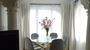Un comedor con una mesa de vidrio, cuatro sillas, un florero con flores y un televisor sobre un mueble de madera.