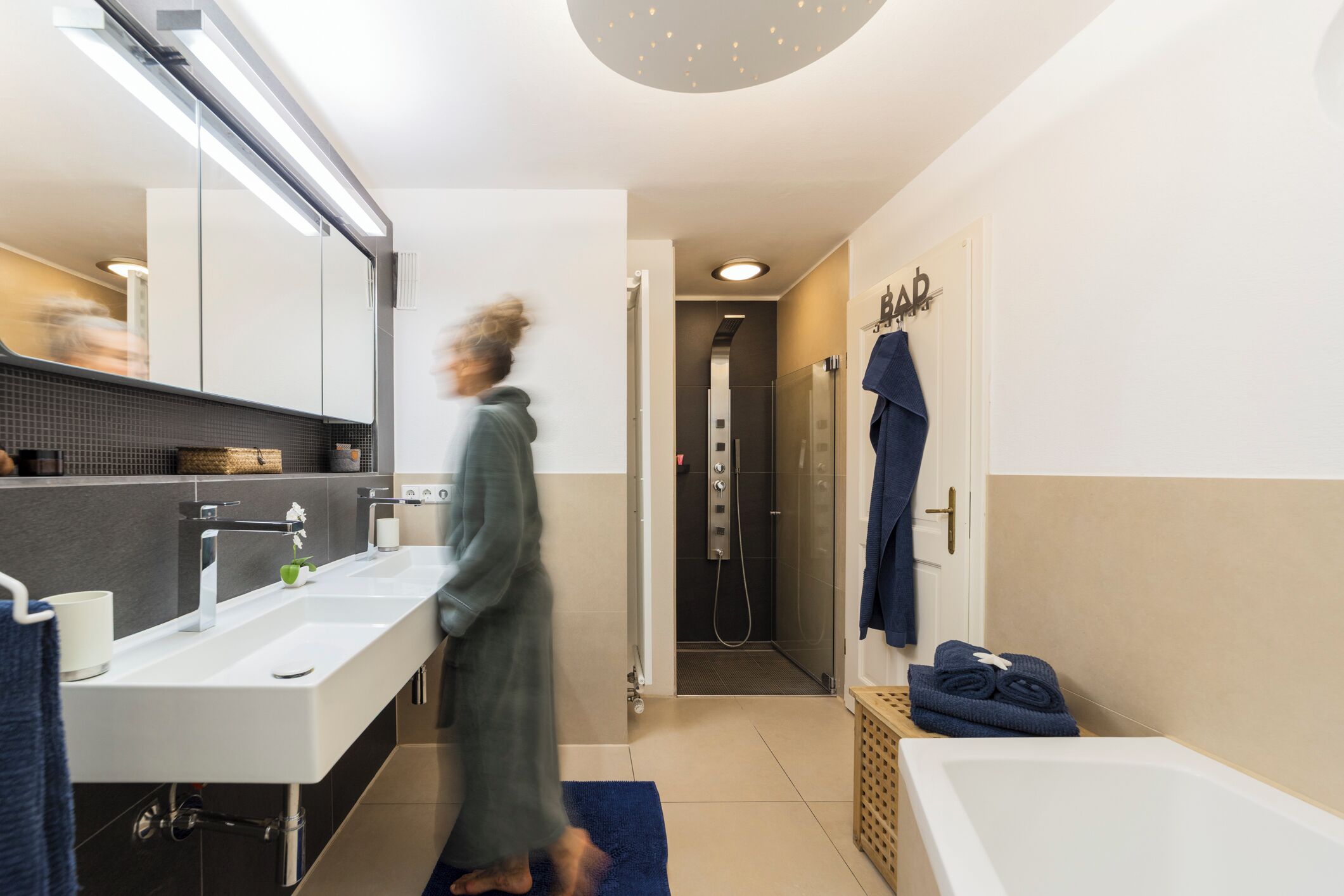 A modern bathroom with a large mirror, two sinks, a shower, and a bathtub.