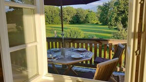 A deck with a table set for dining, overlooking a lush green landscape.