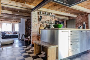 Cozinha com parede de tijolos, eletrodomésticos de aço inoxidável e piso xadrez.