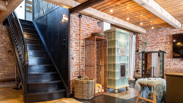 A staircase leading to a loft area with a brick wall, a wooden stool, and a basket on the floor.