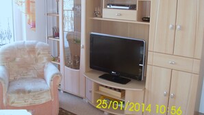 Una sala de estar con televisor sobre un mueble de madera, una silla y un aparador con estantes.