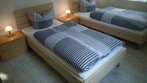 Ein Hotelzimmer mit zwei Einzelbetten, jeweils mit einem Holz-Kopfteil, einem Nachttisch mit Lampe und einem zusätzlichen Tisch.