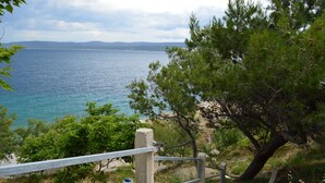 Un sendero costero con una escalera de hormigón que baja a la playa, rodeado de vegetación y con vistas al mar.