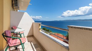 Un balcón con mesa y sillas, con vistas a la costa, cielos despejados y montañas distantes.