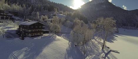 A snow-covered landscape with a mountain, a wooden cabin, and a building with multiple windows.