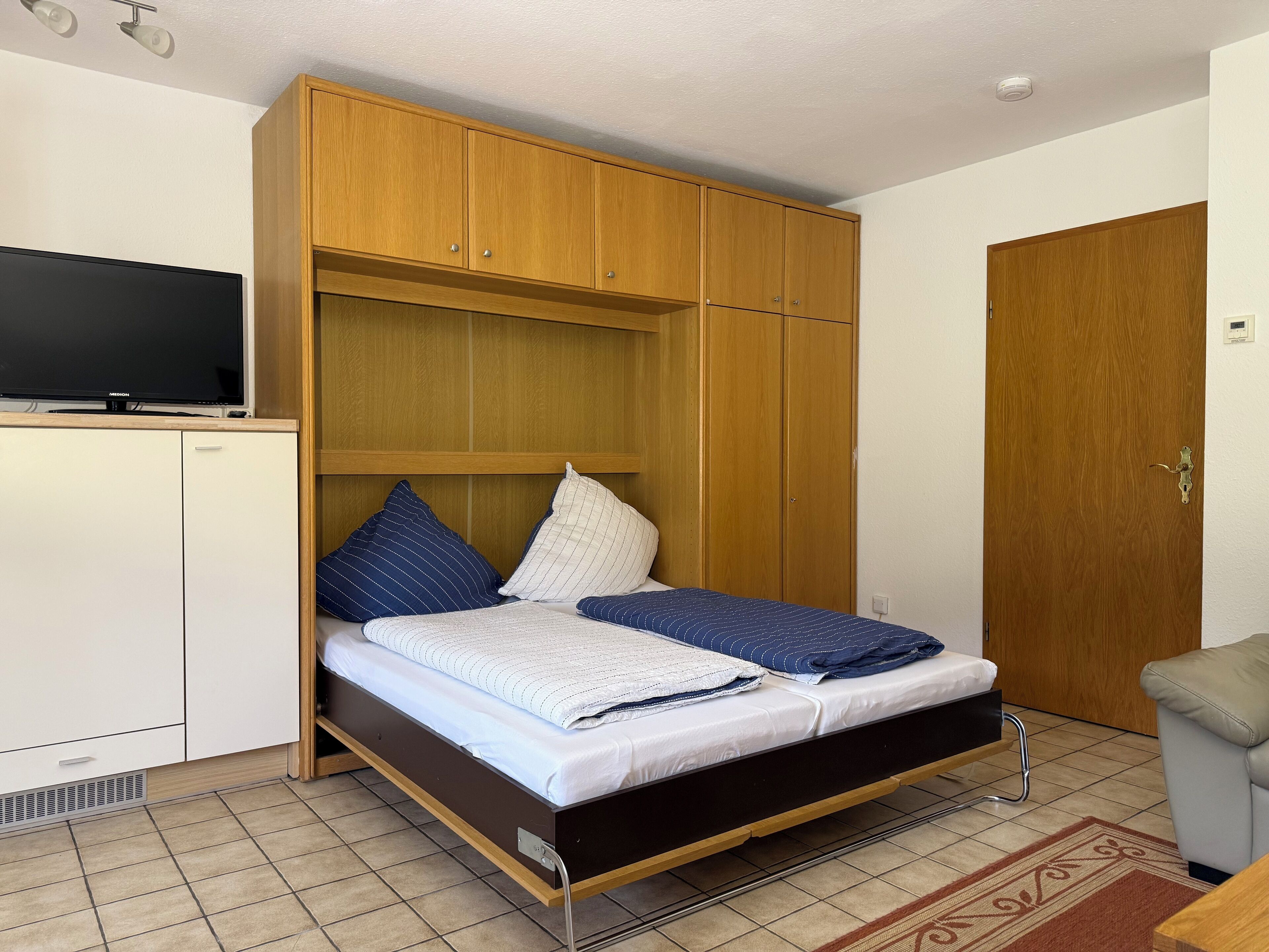 A single bed with a wooden headboard, a television on a cabinet, and a door with a handle.