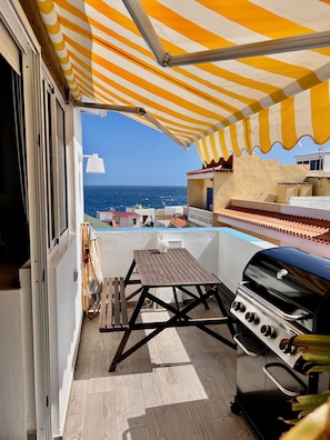 Un balcon avec vue sur la mer, un barbecue et une table.