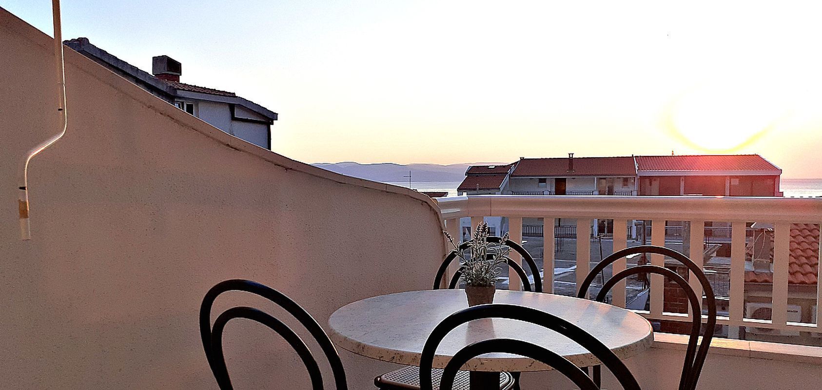 A round table with chairs on a balcony overlooking a sunset.