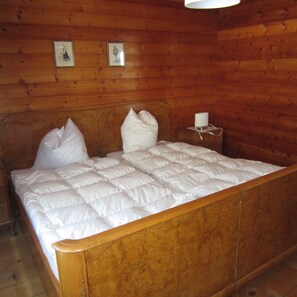 Cozy bedroom with a large bed and wooden ceiling, featuring a bedside table and framed pictures.