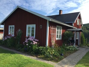 Een rode houten woning met witte details, schoorsteen en een grindpad.