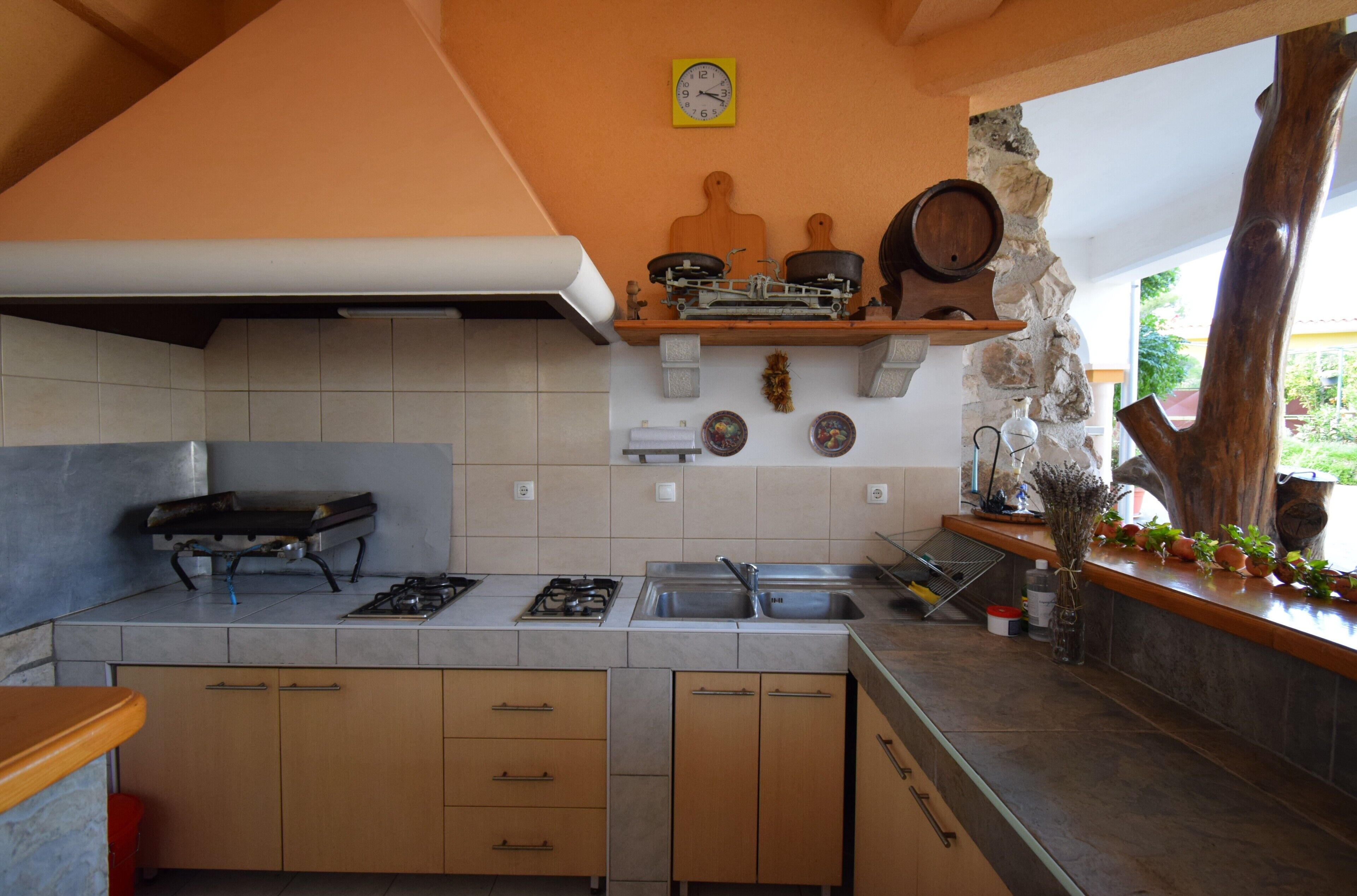 A kitchen with a gas stove, a sink, wooden cabinets, and a stone wall.