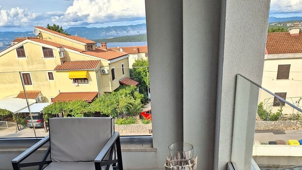 A balcony with a sofa and chairs, a small table, and a decorative item. The balcony overlooks a residential area with buildings and a lake. -  Relax with a view of the sea !! (Vantacici-Malinska)