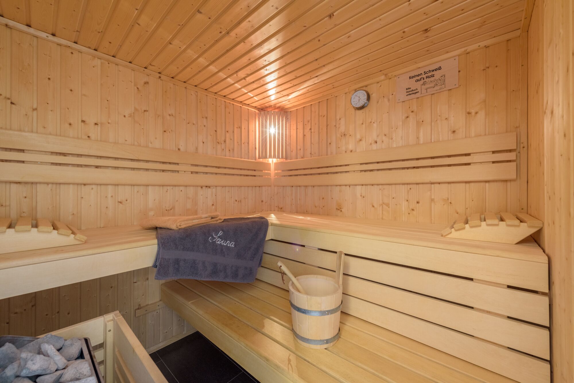 A sauna room with wooden benches, a towel, and a bucket.