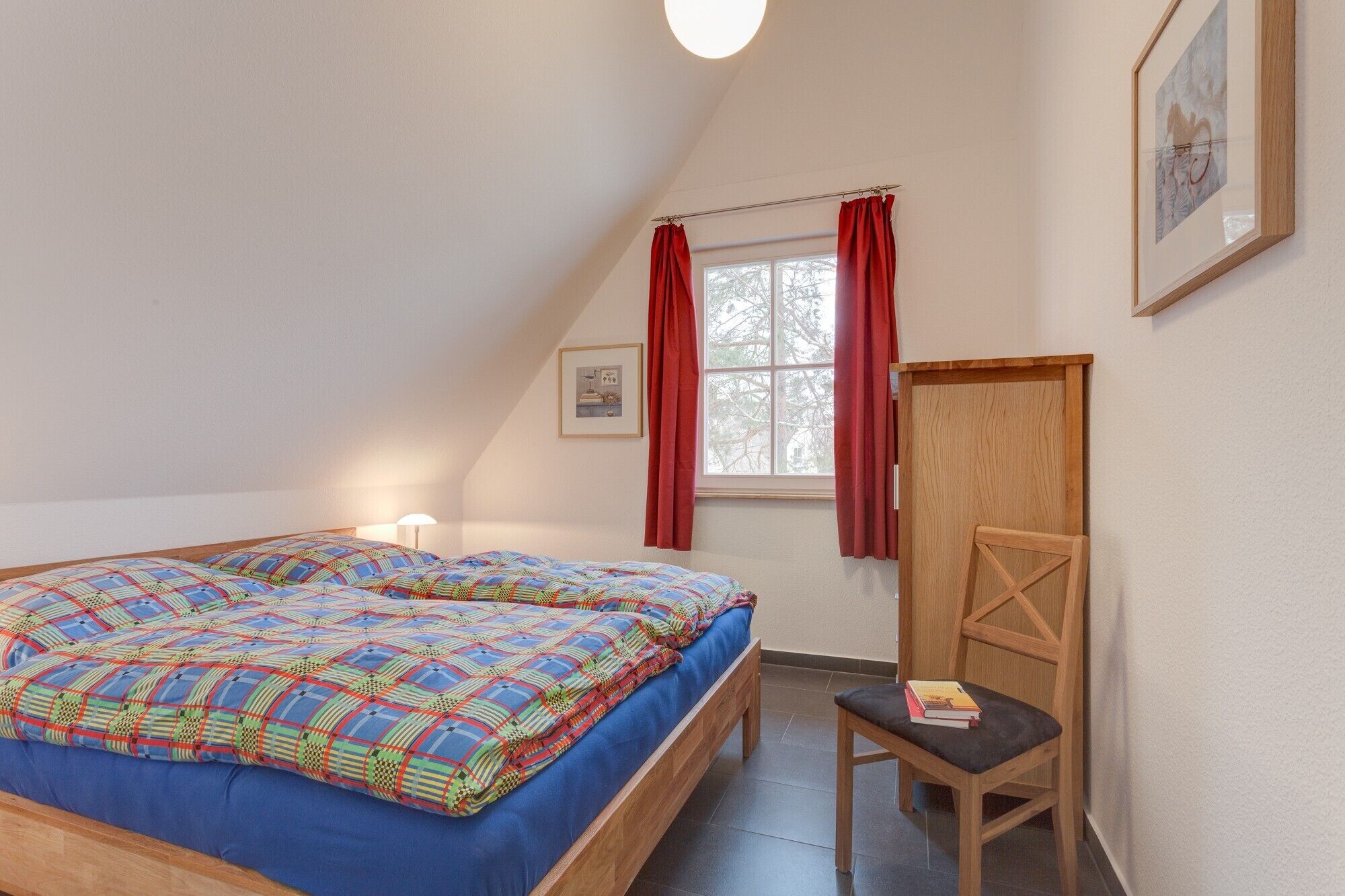 Un dormitorio con cama, una silla, ventana con cortinas y un cuadro en la pared.
