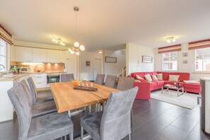 A modern kitchen with white cabinets, a wooden dining table, and a red sofa in the living area. - Close to the beach, quiet, family-friendly, sustainable, sauna, fireplace, garden, e-charging station (Glowe)