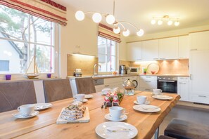 A modern kitchen with white cabinets, a wooden countertop, and a dining area with a wooden table set for a meal. - Close to the beach, quiet, family-friendly, sustainable, sauna, fireplace, garden, e-charging station (Glowe)