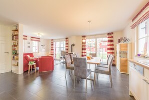 A spacious living area with a red sofa, a dining table with chairs, and a kitchen area with a dishwasher. - Close to the beach, quiet, family-friendly, sustainable, sauna, fireplace, garden, e-charging station (Glowe)