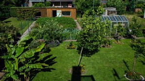 Een modern huis met een verzorgde tuin, inclusief een kas en diverse planten.