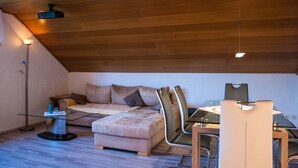 Een gezellig loft slaapkamer met houten plafond, een slaapbank, een eettafel met stoelen, en een projecter bevestigd aan het plafond.