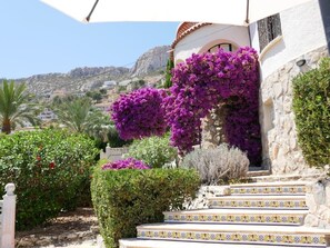 Un bâtiment doté d’une façade en pierre, un escalier menant à une porte, et une vue sur un paysage montagneux en arrière-plan.