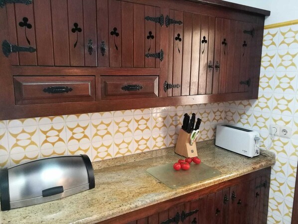 Une cuisine avec des meubles de rangement en bois, un grille-pain et un porte-couteaux contenant des tomates.