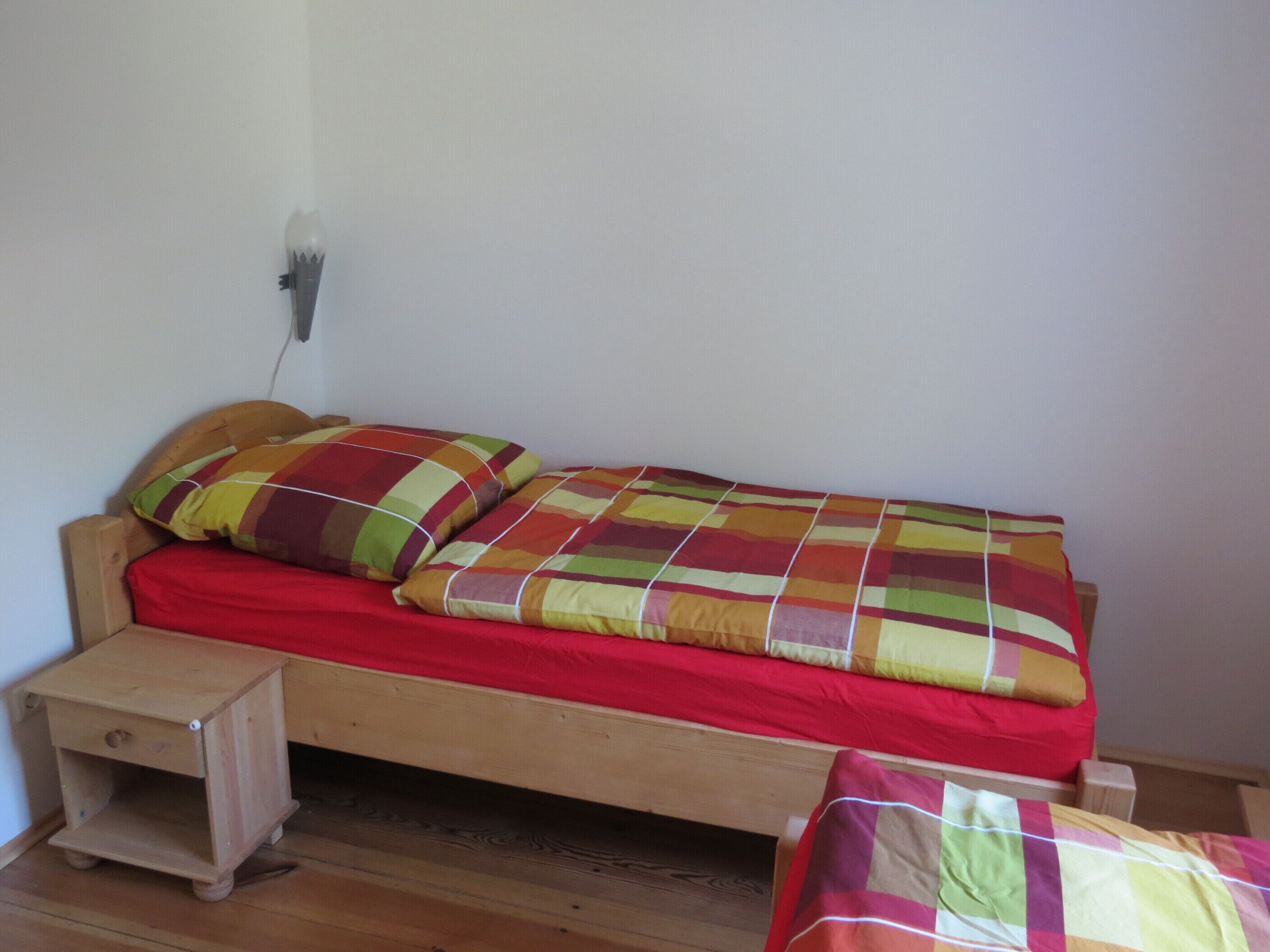 A small wooden bed with a red mattress and colorful striped bedding.