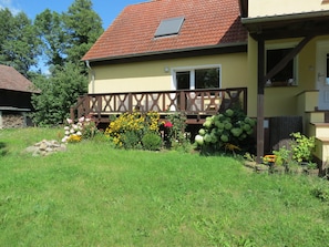 A house with a red-tiled roof, a wooden deck, and a garden with various flowers and plants.