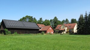 Un paysage rural avec une grange, une maison rouge et une maison jaune dotée de panneaux solaires sur le toit.