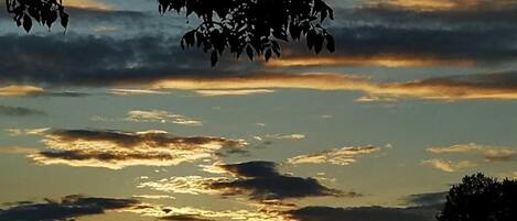 Um pôr do sol com nuvens e silhuetas de árvores.