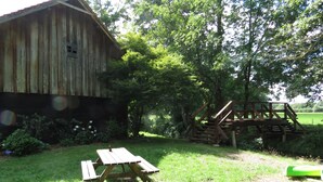 Une grange en bois rustique, une table de pique-nique et un pont en bois, le tout dans un cadre verdoyant et luxuriant.