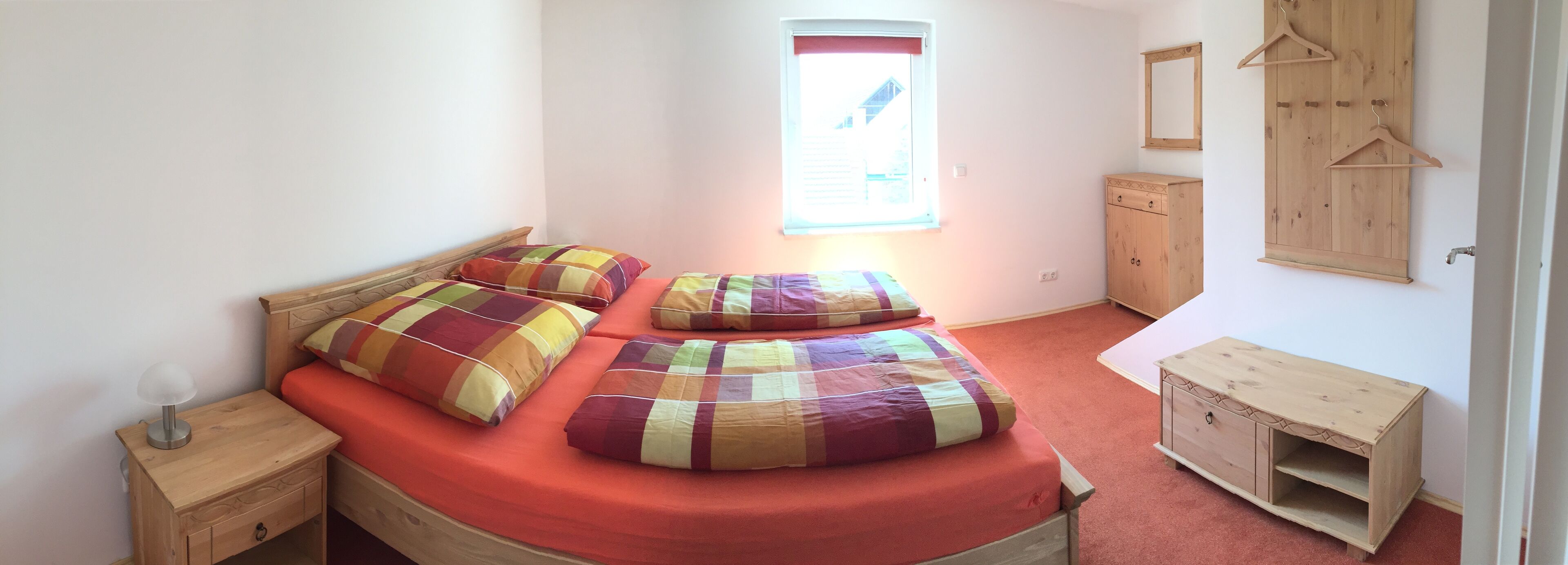 Ein Schlafzimmer mit Bett, Nachttisch, Holzschrank und einem Fenster mit Jalousien.