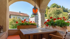 A wooden bench with a cushioned seat under a stone archway, a hanging lantern, and flower boxes with red flowers.