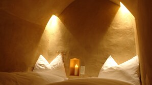 A dimly lit room with a bed, two bedside tables, and a lit candle.