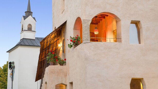 A building with a white facade, a visible bell tower, and a balcony with potted plants.