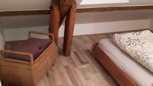 Ein Schlafzimmer im Loft-Stil mit schrägem Dach, einem Holzbett, einem Korbstuhl und einem kleinen Fenster.