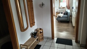 Käytävällä on puinen penkki, pieni pöytä, jossa on kasvi, ja seinällä peili.
