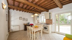 Una cocina con una mesa de comedor, sillas, un frutero, un radiador y una ventana con vista a la vegetación.