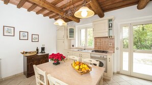 Una cocina con armarios blancos, techo de madera y una mesa de comedor con fruta.
