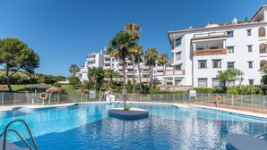 A swimming pool with a circular island, surrounded by a fence, and adjacent to a multi-story building with balconies. - Outdoors apartment labandera at the gates of Marbella (Mijas Costa)