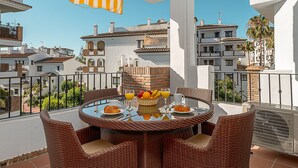 A balcony with wicker furniture, a table with breakfast items, and a view of surrounding buildings. - Outdoors apartment labandera at the gates of Marbella (Mijas Costa)