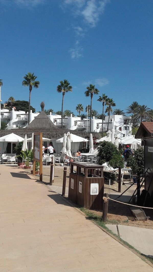 A coastal resort area with white buildings, palm trees, and outdoor seating areas.