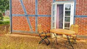 Un bâtiment en briques avec une porte blanche et une petite table accompagnée de deux chaises, le tout placé à l’extérieur.