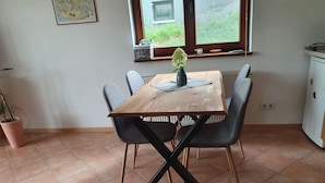 A dining area with a wooden table, four grey chairs, a potted plant, and a window with a view of greenery outside. - Hunsruecklust vacation apartment with e-bike rental (Beltheim)