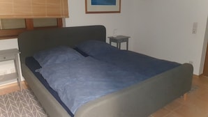 A bedroom with a bed, a nightstand, a small table, and a window with blinds. - Hunsruecklust vacation apartment with e-bike rental (Beltheim)