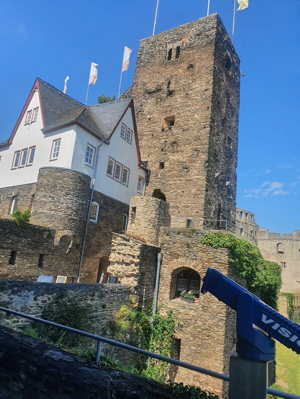 Ein historischer Steinturm neben einem weißen Gebäude mit vielen Fenstern und einem roten Dach.