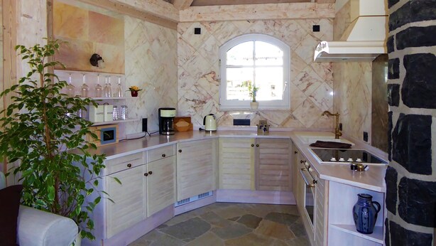 Une cuisine avec un sol en pierre, des poutres en bois au plafond, une grande fenêtre et un mur en pierre.