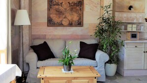 Un salon avec un canapé beige, deux coussins noirs, une table basse en bois ornée d’une plante, une plante en pot et un meuble contenant de la verrerie.